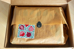 Unwrapping a tissue paper wrapped knit blanket with a pomegranate design